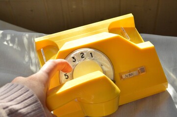 A person dials a number on a vibrant yellow vintage rotary phone, capturing the essence of a bygone...