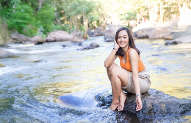 Asian woman meditating on a rock surrounded by a flowing stream and verdant forest