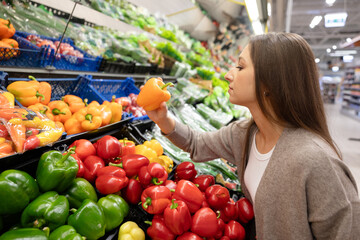 Woman selecting fresh yellow bell peppers in the vegetable section of a supermarket. Concept of healthy eating, buying natural products, and caring about food quality.