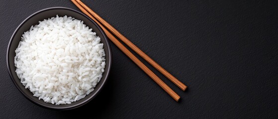 Overhead View of Cooked Rice in a Black Bowl with Chopsticks on a Dark background. 