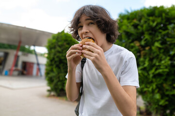 Hungry student eating burger for lunch and looking happy