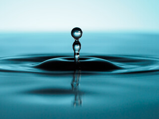 two blue water droplets on light blue background floating in the air in equilibrium over a water...