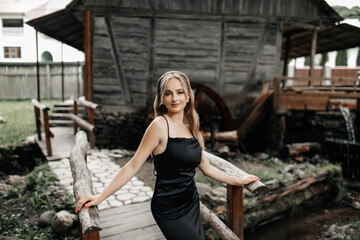 woman standing on a wooden bridge. She is wearing a long black dress and white high heels.
