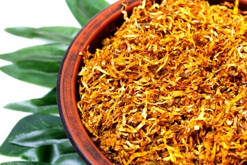 Fermented yellow tobacco in a brown plate on a white background with green leaves