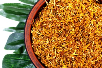 Fermented yellow tobacco in a brown plate on a white background with green leaves