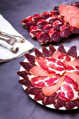 Sliced meat on a plate, knife and tongs on a white napkin, on a gray background
