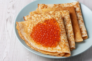 Savory crepes filled with fresh orange fish roe served on a light blue plate at a cozy breakfast table