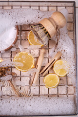 Close-up of natural fiber brush, dishwashing foam, lemon wedges, top view