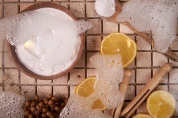 Close-up of natural fiber brush, dishwashing foam, lemon wedges, top view