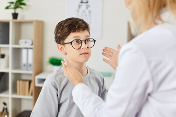 Ophthalmologist in the clinic examines a boy wearing glasses for vision, close-up. The child looks...