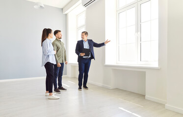 Young couple tours a new home with a real estate agent or realtor, preparing for purchase or rent....