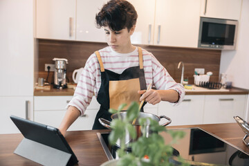 Teenager girl preparing meal while following instructions on a tablet, showcasing modern cooking habits