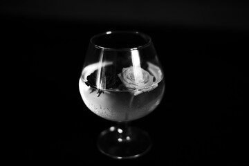 A glass of water with roses captured in soft sunlight, with a black-and-white palette highlighting elegance and timeless beauty.