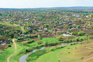 Fototapeta premium Aerial view of Furceni village in Moldova featuring traditional houses and lush green fields, with winding Raut river adding picturesque landscape. Rural setting is complemented by surrounding hills 