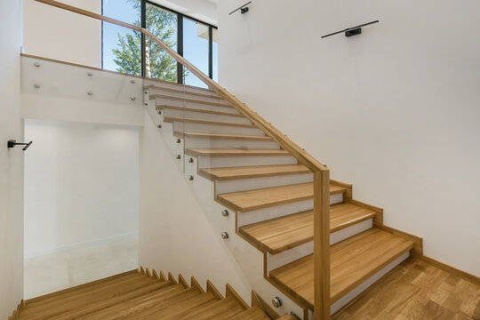 A staircase with light wood steps and glass railings, in the lobby of a luxurious house.