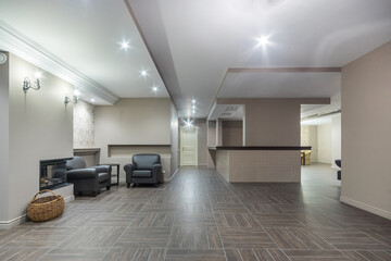 Spacious living room with fireplace and leather armchairs in a luxurious chalet. Room decor in pastel colors, tiled floor.