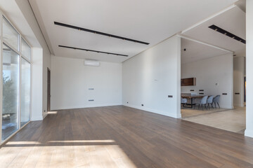 An empty living room with panoramic windows in a luxurious mansion. Parquet floor, light decor. Unfurnished.