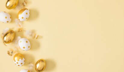 Festive gold patterned Easter eggs and feathers scattered on a light background. Beautiful background with Easter eggs and space for text.