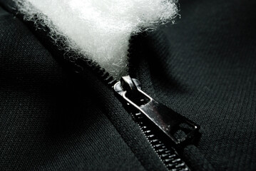white synthetic non-woven holofiber fabric is sticking out through the zipper of black clothing