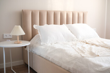 A cozy bedroom with a beige headboard, fluffy pillows, and soft decor accents for a serene atmosphere.