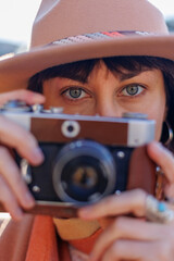 Fashionable look, young woman with a film camera wearing an elegant hat and coat. A hipster tourist...