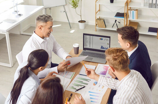 Business team doing data analysis during work meeting. Group of people sitting together at office table, discussing professional marketing tools, using laptop computer, and drinking coffee - Powered by Adobe