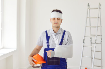 Injured worker in uniform after accident standing on construction site with arm in plaster cast and...