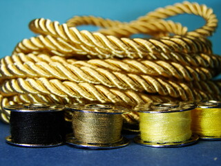 Kolorowe nici na szpulkach widoczne na tle złotego, grubego sznurka