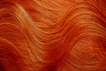 Red hair close-up as a background. Women's long orange hair. Beautifully styled wavy shiny curls. Hair coloring bright shades. Hairdressing procedures, extension.