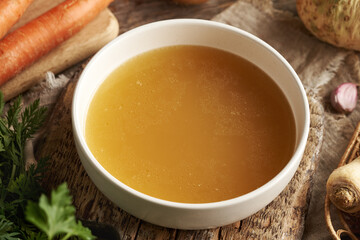Chicken soup or bone broth in a white ceramic bowl on a table