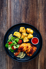 Oven roasted chicken thigh with potatoes and fresh salad on wooden table