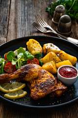 Oven roasted chicken thigh with potatoes and fresh salad on wooden table