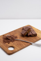 Spoon with cocoa powder and delicious chocolate with filling on table, top view. Milk, dark chocolate bar

