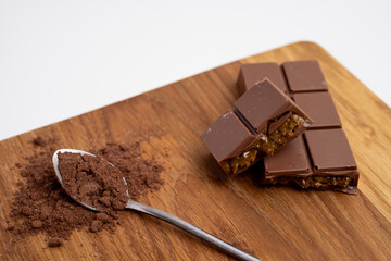 Spoon with cocoa powder and delicious chocolate with filling on table, top view. Milk, dark chocolate bar
