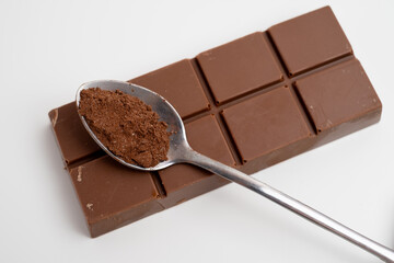 Spoon with cocoa powder and delicious chocolate with filling on table, top view. Milk, dark chocolate bar