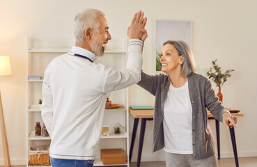 Obraz premium Smiling elderly senior couple giving high five to each other rejoicing success standing in living room at home. Retired man and woman are happy with good news. Relationship in retirement concept.