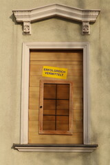 Window on a building is boarded up with wooden boards. The sign reads "ERFOLGREICH VERMITTELT", which is German for "successfully brokered".