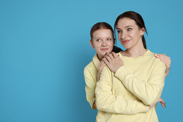 Portrait of beautiful mother with teenage daughter on light blue background, space for text