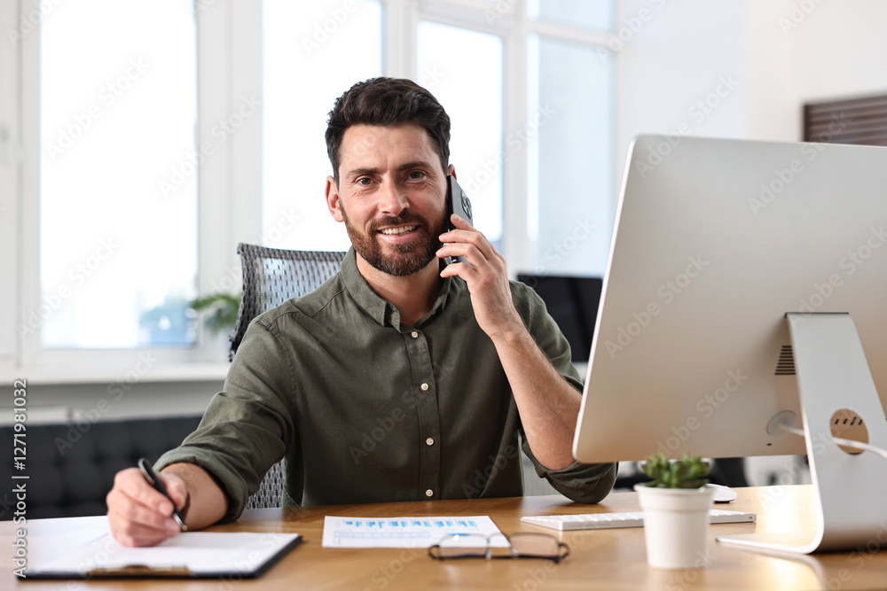 Poster man talking on smartphone while working at table in office
