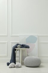 Knitted pouf, fuzzy slippers and decor elements near white wall indoors. Space for text