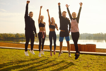 Portrait of a happy sporty people wearing sportswear jumping in a row with hands up on the lake...