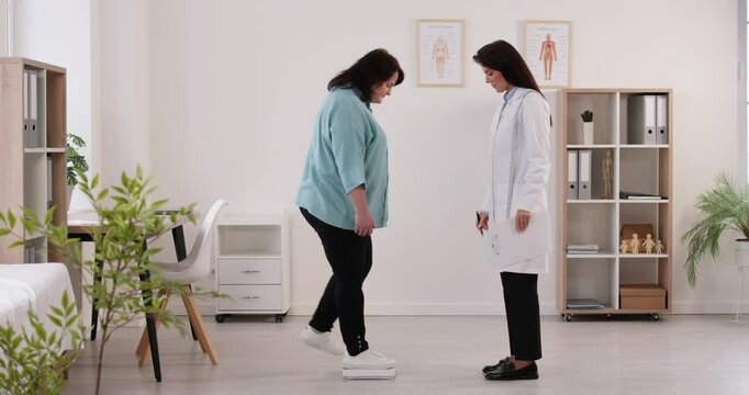 Process of weighing chubby woman on floor scale in presence of nutritionist. Female nutritionist doctor observes overweight woman and then shakes her hand after successful consultation. Video footage.