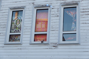 ISTANBUL, TURKEY, 2019: Three windows of an old building. The exterior walls are made of peeling white painted wood. Each window has curtains hanging inside, different colors and patterns.