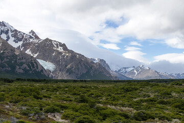 Beautiful landscape with contrasting colors of lush green vegetation, snowy mountains, blue sky and clouds