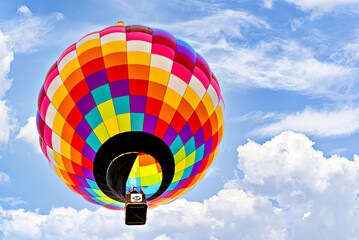 Colorful hot air balloon flying over blue sky with white clouds	