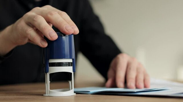 Close-up Of A Man's Hand Stamping With Approved Stamp On Document At Desk. Man Border Control Officer Puts a Stamp in the International Passport