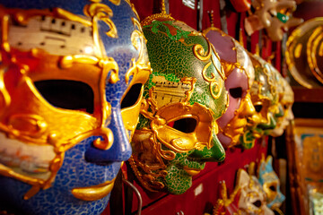 A close-up picture of several masks prepared for festival in Venice. masks are hаng on wall in row, waiting for people who to wear them. They are made from several layers of paper and painted in color