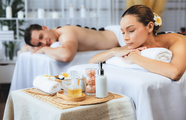 Hot stone massage at spa salon in luxury resort with day light serenity ambient, blissful couple customer enjoying spa basalt stone massage glide over body with soothing warmth. Quiescent