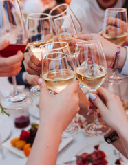 Group of guests celebrate and raise glasses, toasting and cheering with alcohol glasses with wine and champagne in a restaurant on corporate christmas, birthday party prom event or wedding celebration © tsuguliev