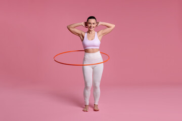 Smiling woman training with hula hoop on pink background